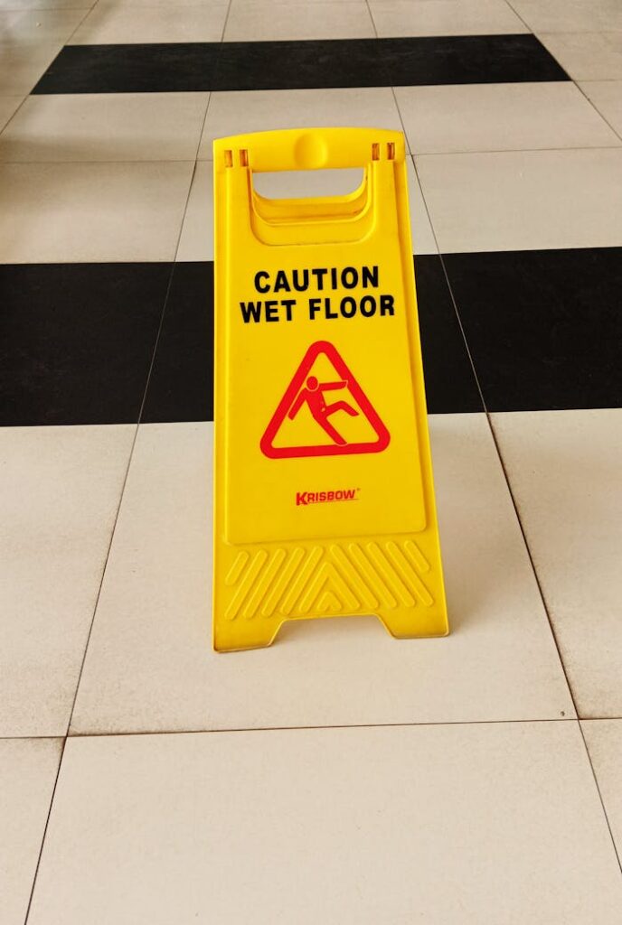 Vibrant yellow caution wet floor sign on black and white tiled floor indoors.